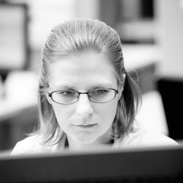 Professional woman with glasses focused on computer work, testimonial headshot
