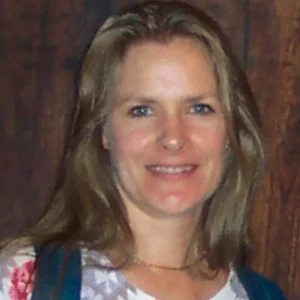Smiling woman with long blonde hair in front of wooden wall, testimonial photo