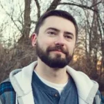 Man with beard and hoodie in a wooded area, casual testimonial headshot